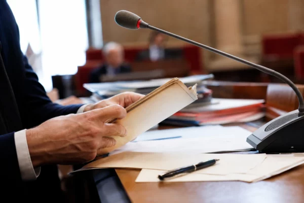Mains anonymes manipulant un dossier devant un micro de commission dans une salle parlementaire