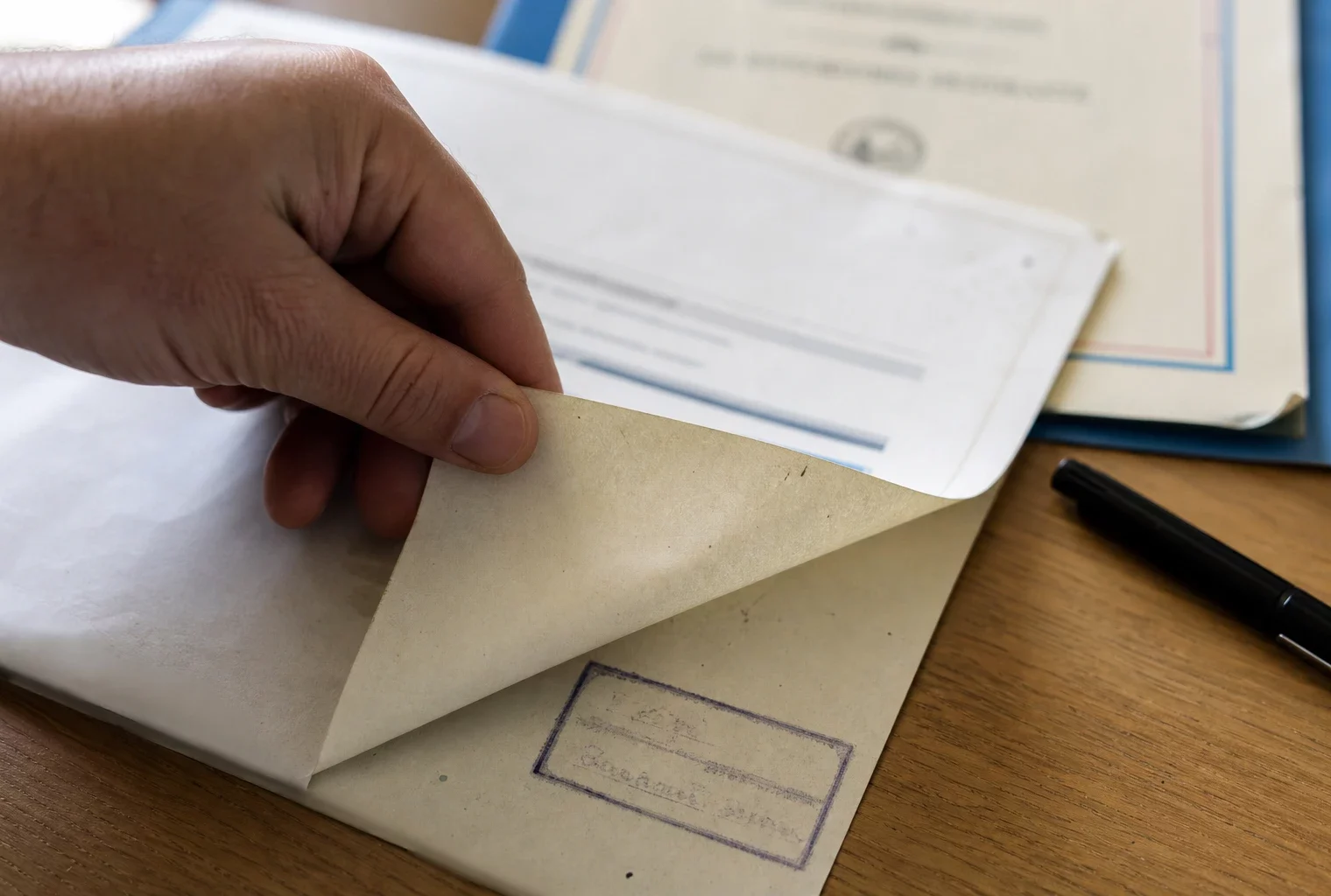 Main tournant un dossier de finances publiques sur un bureau en bois, sous une lumière de fenêtre claire.