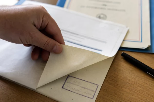 Main tournant un dossier de finances publiques sur un bureau en bois, sous une lumière de fenêtre claire.