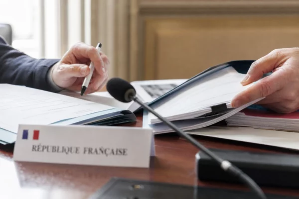 Mains anonymes triant un dossier de nomination avec micro de commission dans une salle institutionnelle française