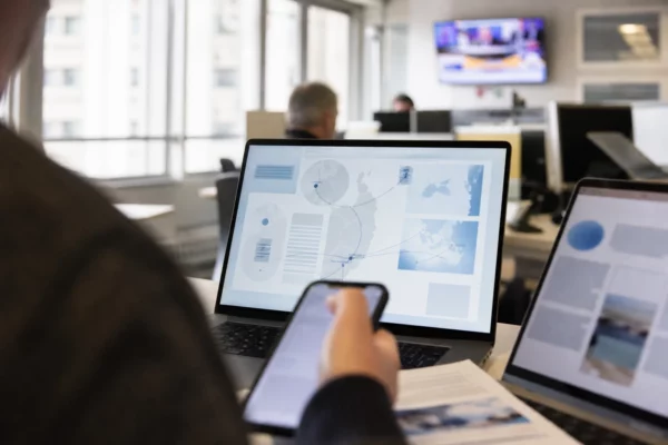 Vue d’ordinateur dans une rédaction parisienne, avec main floue au premier plan et interface abstraite à l’écran.