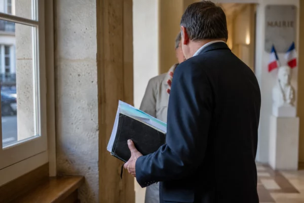 Élu local de dos dans un couloir de mairie, carnet à la main, en discussion avec un habitant.