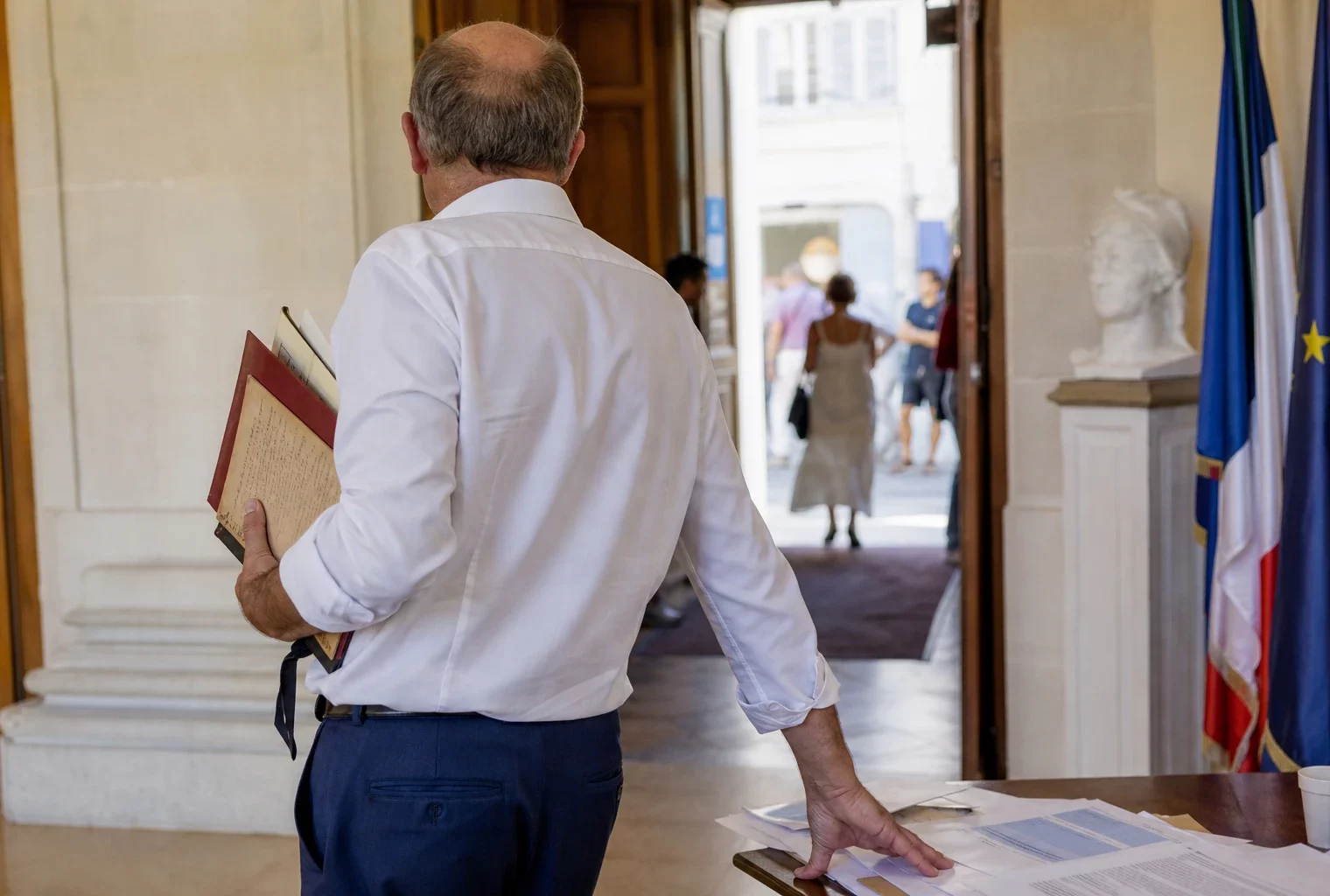 Élu local anonyme vu de dos dans une mairie, carnet à la main, en contexte de débat sur la canicule.