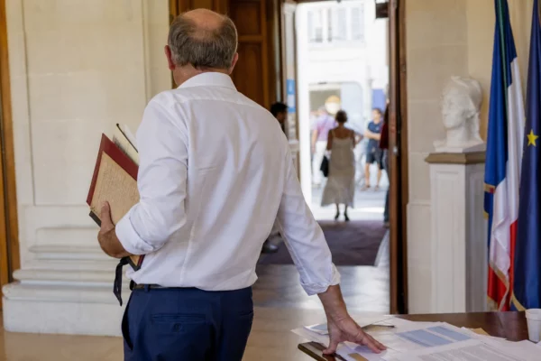 Élu local anonyme vu de dos dans une mairie, carnet à la main, en contexte de débat sur la canicule.