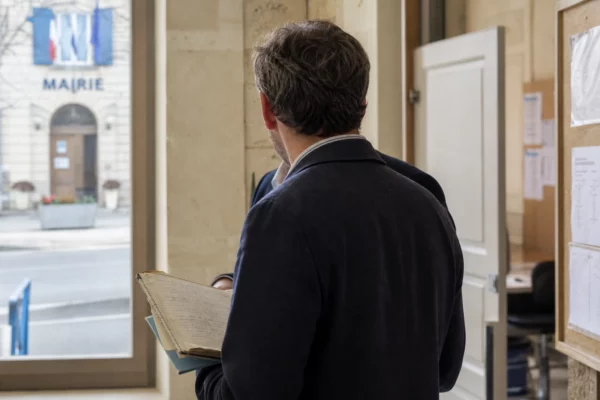 Élu local anonyme de dos dans une mairie française, carnet à la main, avec la rue visible en arrière-plan.