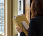 Aide municipale anonyme de dos tenant un dossier dans une mairie de ville française, lumière naturelle et rue en arrière-plan