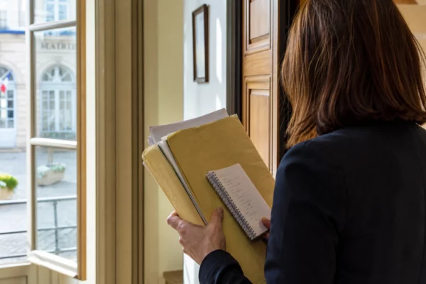Aide municipale anonyme de dos tenant un dossier dans une mairie de ville française, lumière naturelle et rue en arrière-plan