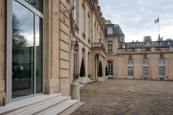 Cour intérieure de l’Élysée vide, en lumière naturelle, avec marbre clair et drapeau tricolore discret au loin