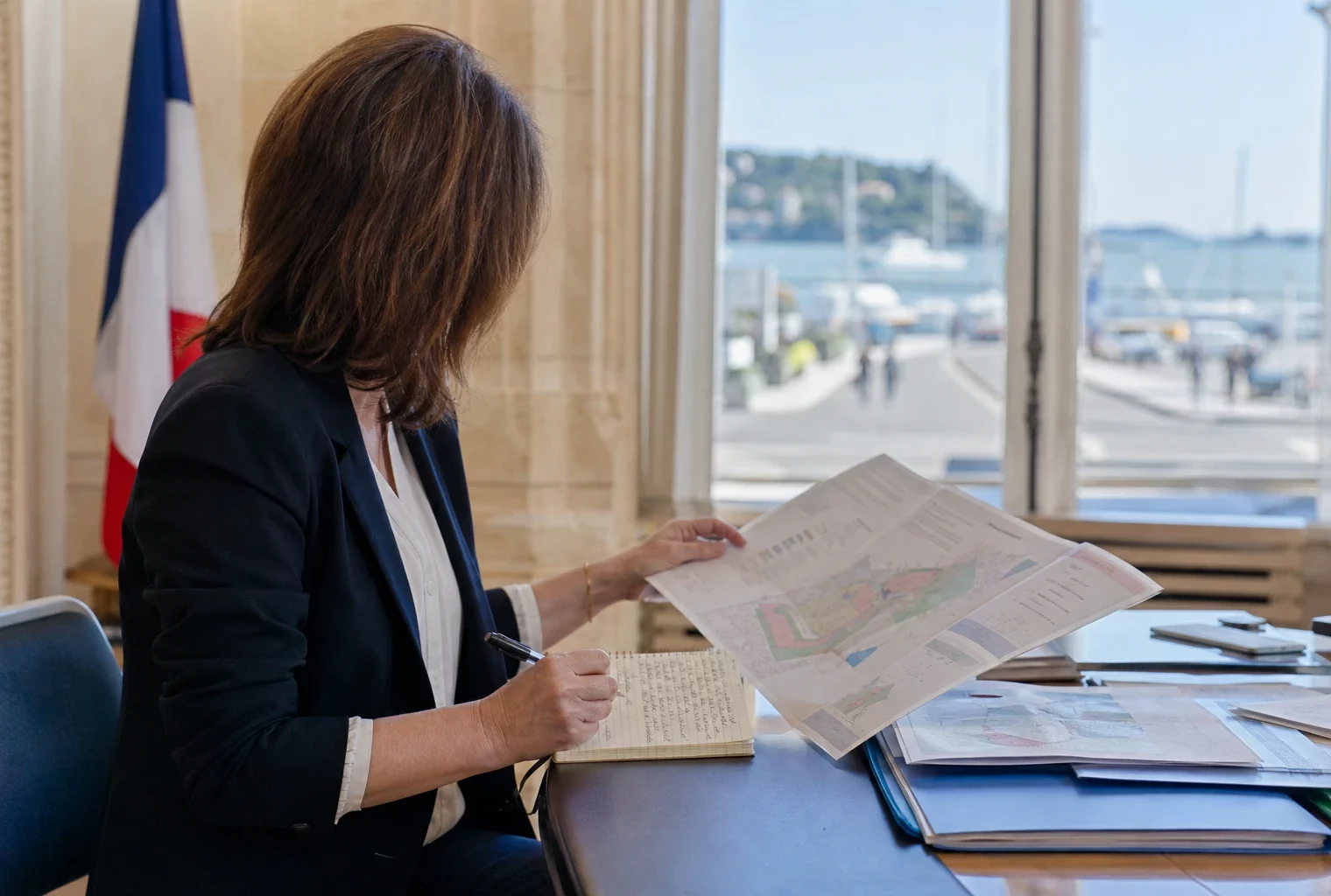 Un élu local anonyme consulte un dossier sur l’éolien en mer dans une mairie lumineuse près du littoral.