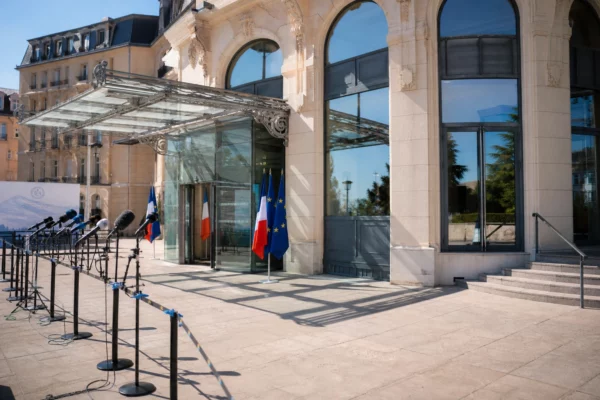 Façade claire du lieu du G7 à Évian avec micros de presse au premier plan et ambiance institutionnelle calme