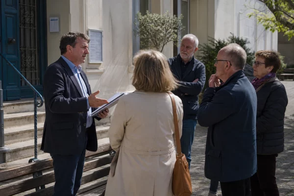 Des habitants et un élu local anonymes échangent devant la mairie sur fond de dossiers et de préoccupations budgétaires.
