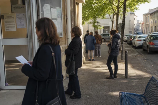 Des patients attendent devant un centre médical de ville moyenne française, dans une rue calme en plein jour.