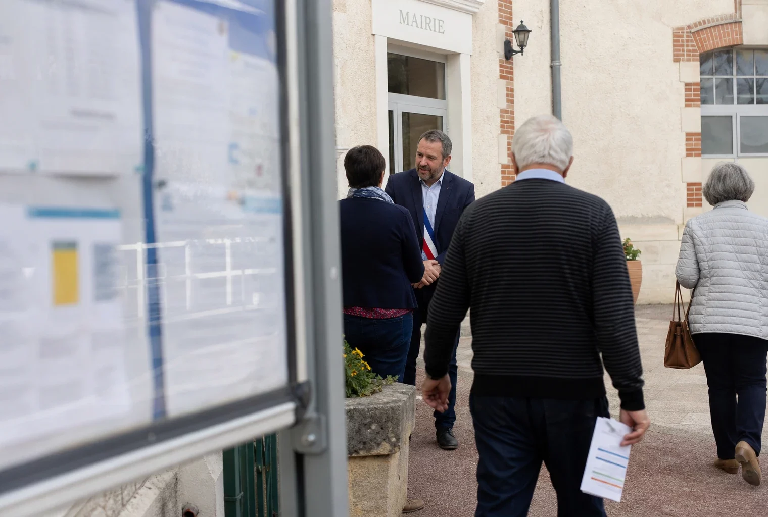 Des habitants et un élu local se croisent devant une mairie de quartier, dans une scène citoyenne lumineuse.