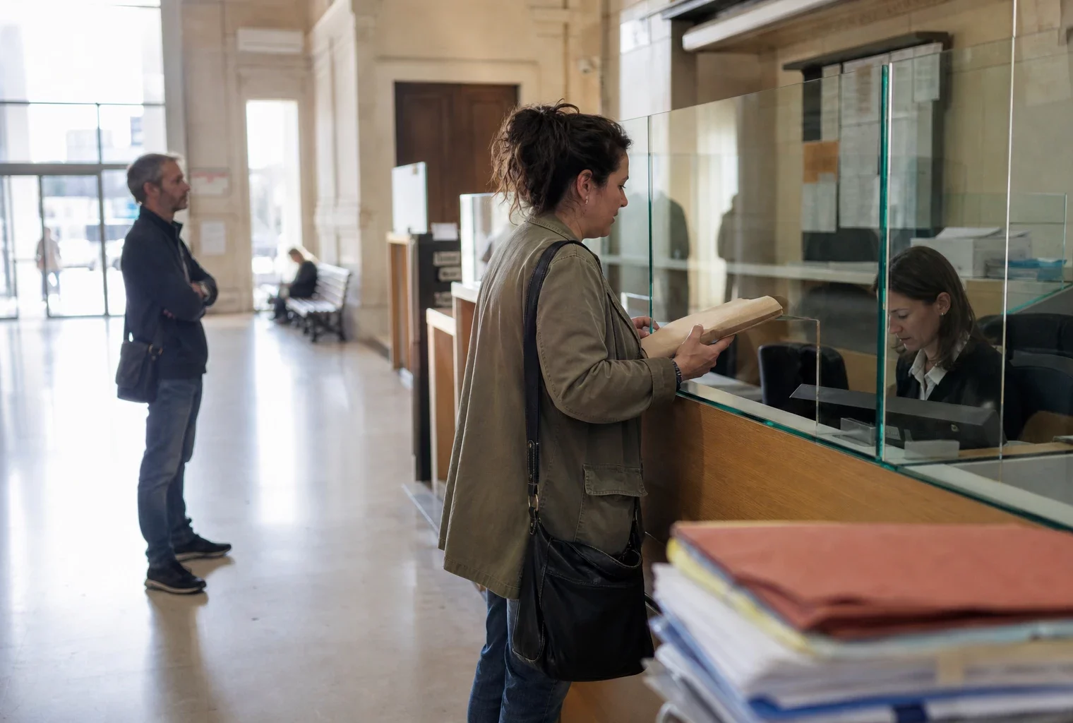 Accueil administratif lumineux avec un dossier au guichet et des usagers anonymes dans un cadre judiciaire français.