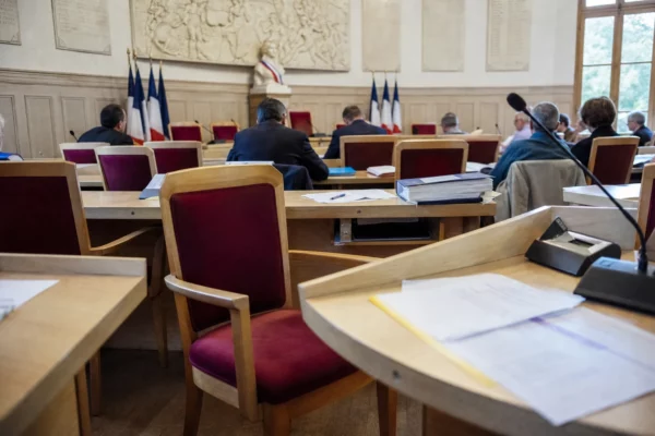 Salle municipale française avec chaises vides, micros et dossiers flous dans une ambiance parlementaire calme.