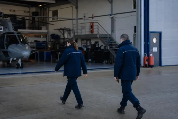 Deux agents anonymes près d’un hangar de gendarmerie, dans une scène calme et documentaire au matin.