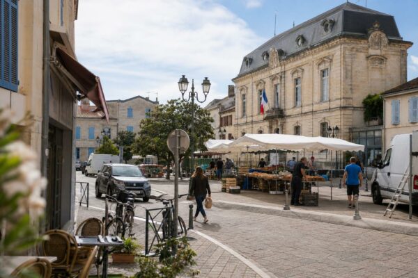 Place de commune française avec marché, mairie et habitants anonymes dans une ambiance de reportage naturel.