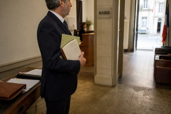 Portrait d’un élu local anonyme dans un couloir lumineux de mairie, dossier à la main, ambiance de succession municipale.