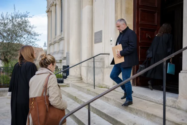 Devant un palais de justice français, des personnes anonymes arrivent avec des dossiers sous une lumière naturelle claire.