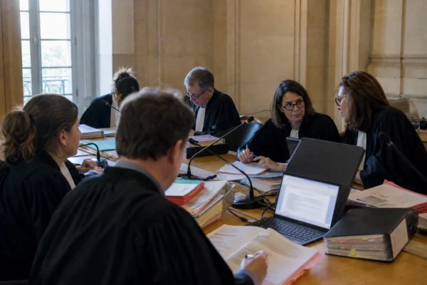 Réunion de magistrats et greffiers dans un tribunal français, dossiers ouverts et écrans flous sur la justice numérique.