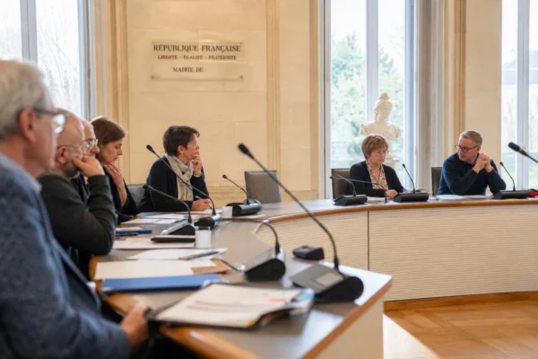 Salle municipale lumineuse avec chaise vide, micros et dossiers flous, ambiance de conseil local en France.