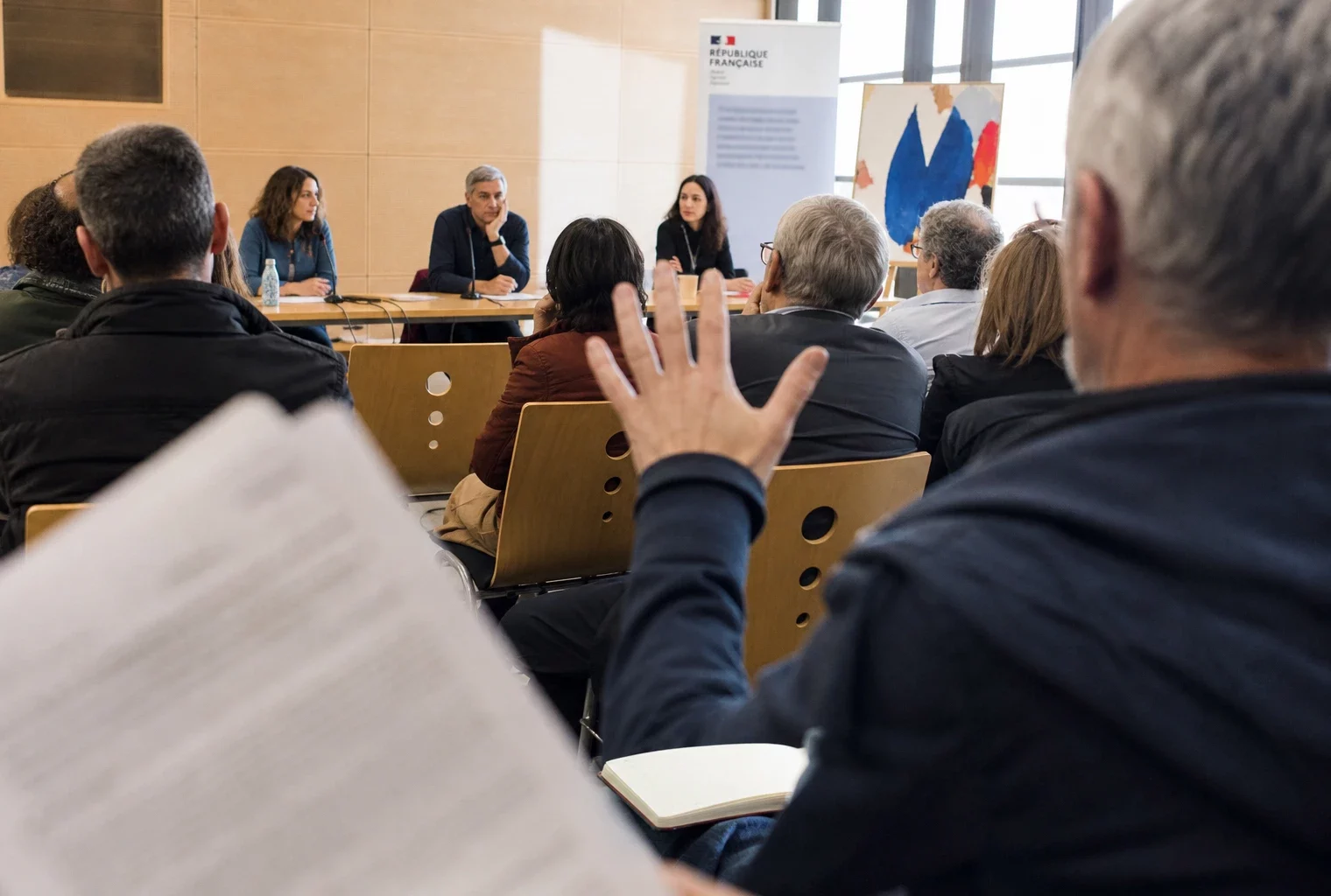 Débat citoyen dans une salle publique française avec micro, document juridique flou et pancarte abstraite