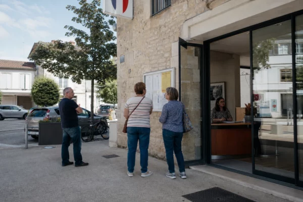 Des citoyens et un agent municipal devant une mairie française, scène de vie publique en lumière naturelle.