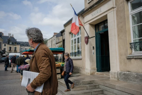 Scène de rue dans une ville moyenne française devant la mairie, avec passants anonymes et marché de quartier.
