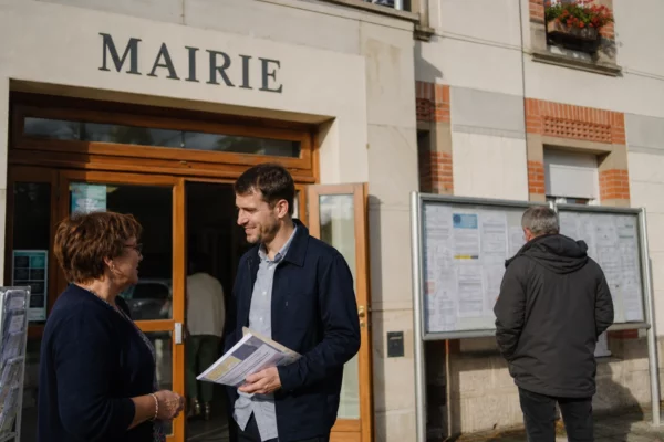 Des habitants discutent devant une mairie française avec des documents floutés, dans une scène de vie citoyenne locale.