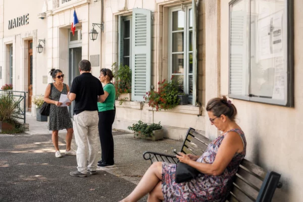 Des habitants attendent devant une mairie française lors d’une journée de forte chaleur et d’adaptation locale.