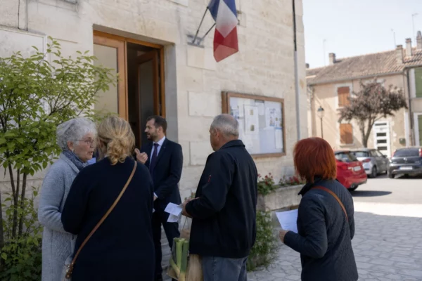 Des habitants discutent devant une mairie de province, dans une scène claire sur l’impact des prix de l’énergie.
