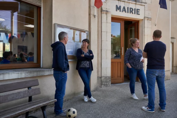 Des habitants discutent devant la mairie d’une petite commune française, dans une scène de vie locale liée au Mondial.