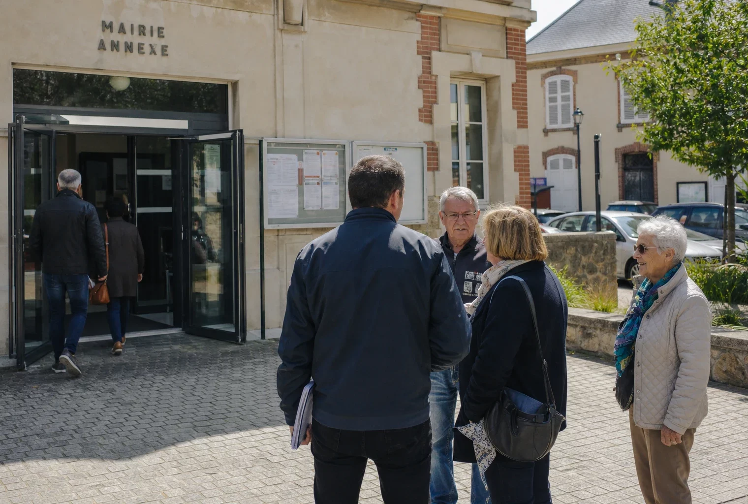 Devant une mairie de ville française, des habitants et un élu local anonyme discutent dans une ambiance de quartier lumineuse.