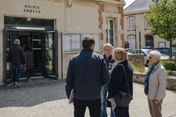 Devant une mairie de ville française, des habitants et un élu local anonyme discutent dans une ambiance de quartier lumineuse.