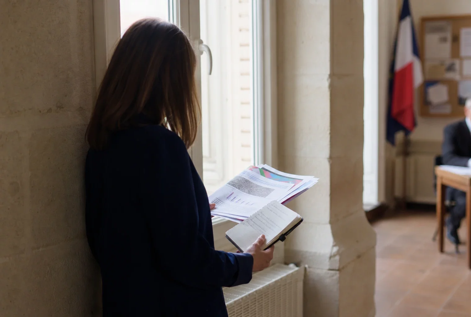 Un collaborateur municipal anonyme consulte un dossier dans une mairie française, en lumière naturelle.