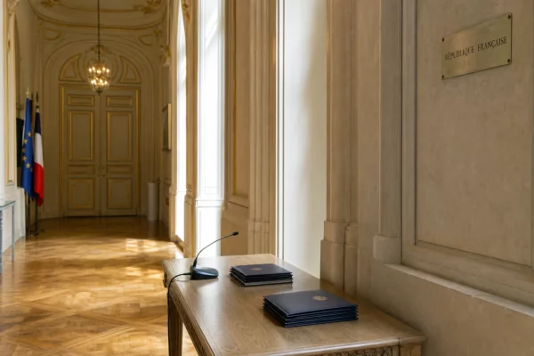 Couloir institutionnel de Matignon avec dossiers de briefing, lumière naturelle claire et ambiance gouvernementale sobre.
