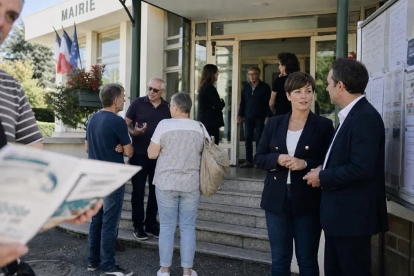 Des habitants et élus anonymes discutent devant une mairie de banlieue française après un meeting local.