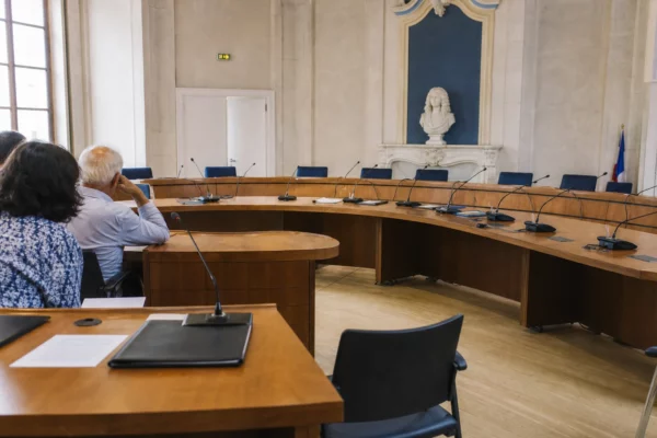 Salle municipale lumineuse avec micros, dossiers et chaise vide pour illustrer la bataille de la gauche en 2027