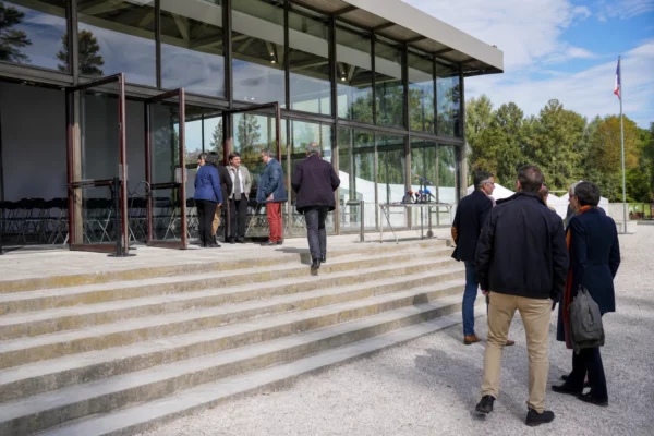 Entrée vitrée d’un lieu de meeting à Paris, avec quelques arrivants et une ambiance politique claire et documentaire.