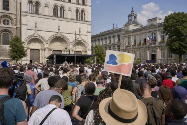 Foule rassemblée à Saint-Denis sur une place urbaine, avec la basilique et l’hôtel de ville en arrière-plan.