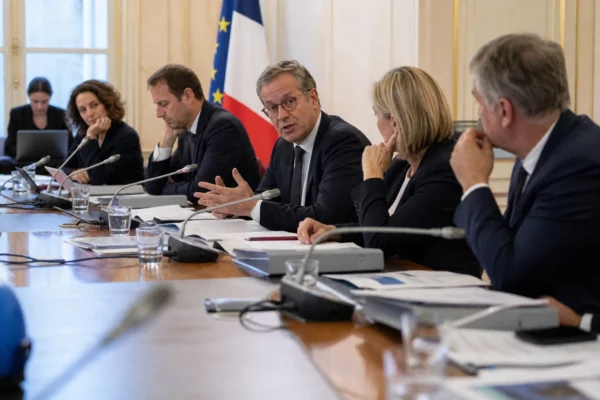 Réunion de ministres et d’aides autour d’une table à l’Assemblée, dans une ambiance budgétaire tendue.