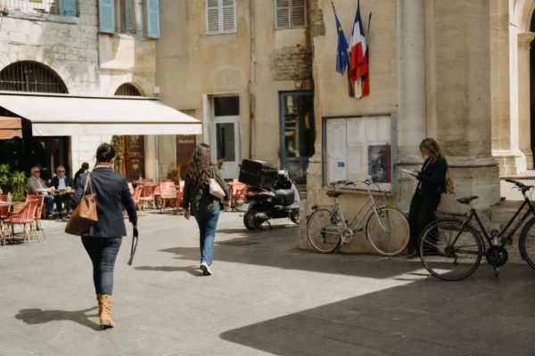 Scène de rue à Nice près d’une mairie, avec habitants anonymes et journaliste en reportage.