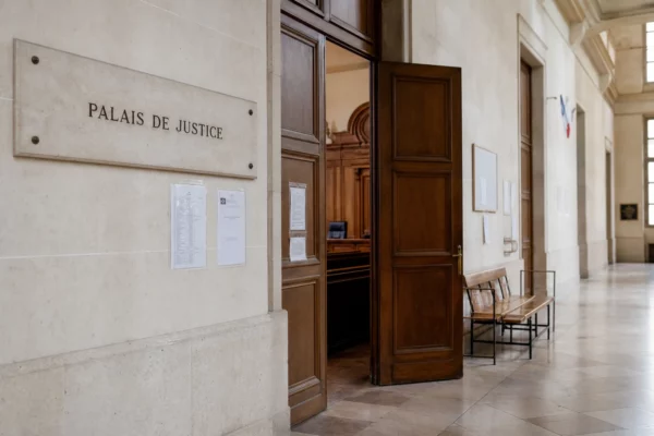 Couloir clair d’un palais de justice français avec porte sobre et salle d’audition en arrière-plan.