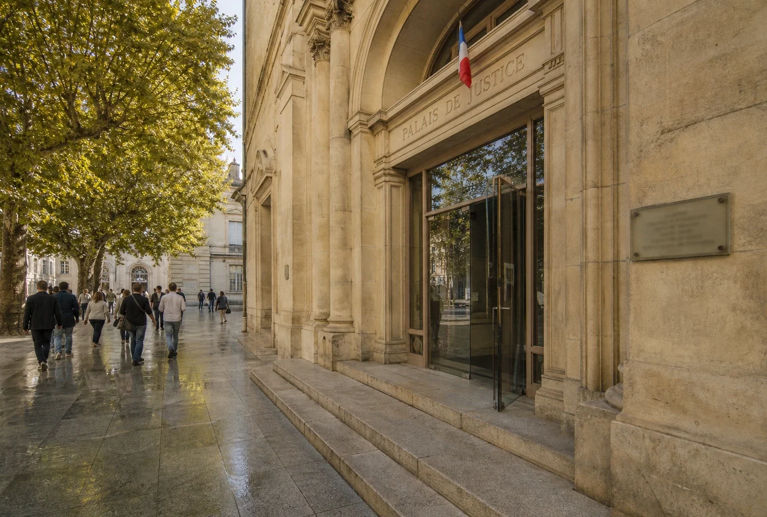 Façade d’un palais de justice français au soleil, avec quelques passants anonymes devant l’entrée