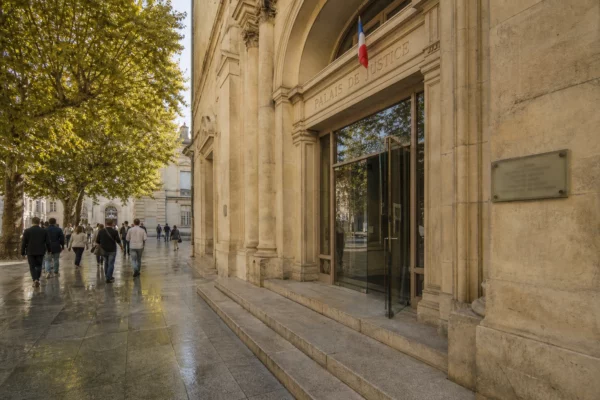 Façade d’un palais de justice français au soleil, avec quelques passants anonymes devant l’entrée