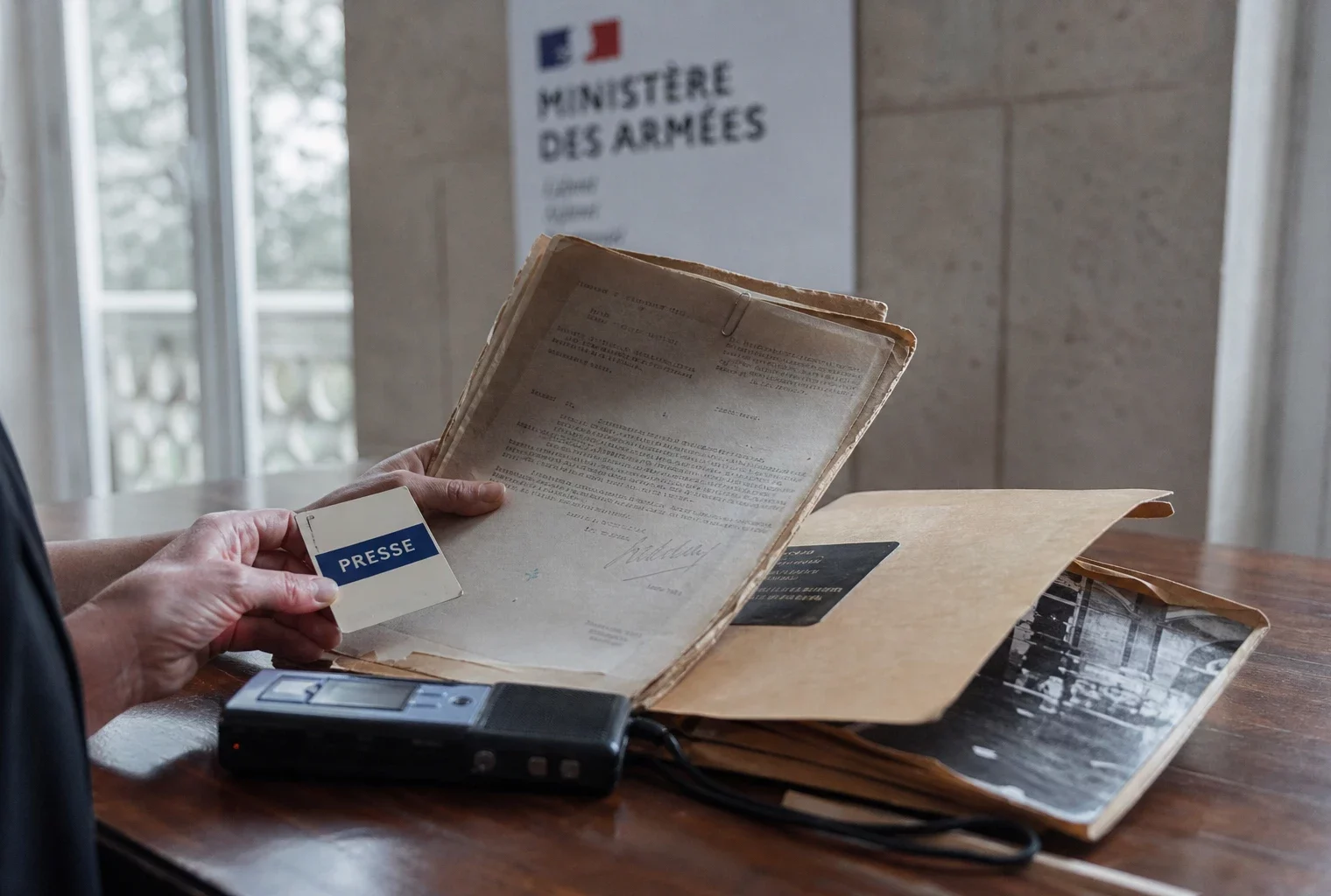 Main tenant un dossier d’archives et un badge générique dans un bureau institutionnel lumineux, en contexte Panthéon.