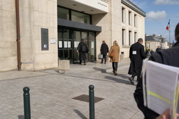 Devant un palais de justice français, des anonymes se croisent dans une scène calme de reportage en lumière du jour.