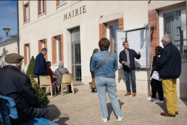 Des habitants anonymes échangent devant une mairie française, sur un parvis lumineux et calme.