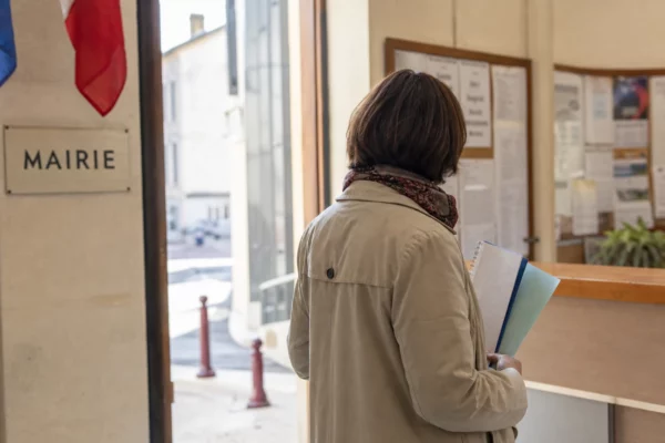 Un collaborateur municipal anonyme de dos tient un dossier dans une mairie française lumineuse.