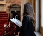 Conseiller parlementaire anonyme avec dossier dans un couloir lumineux de l’Assemblée nationale, sièges rouges flous en arrière-plan